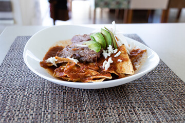 Traditional mexican breakfast chilaquiles with steak served on a curved white plate