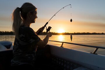Obraz premium A woman on a fishing trip caught a fish.Fishing on the lake from a boat. Fishing rods in sunlight. Fishing rest concept. 