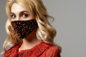 Woman wearing stylish dark red velvet protective face mask with golden rhinestones, beads. Fashion...