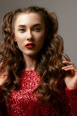 Fototapeta premium Close up beauty portrait of young attractive brunette woman with eyelines, red lips makeup, long waved hair, posing in studio, on gray background