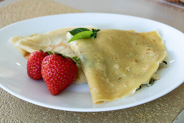 Close up of crepes with strawberries served on a white plate
