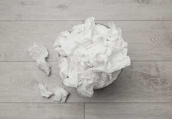 Used paper tissues and trash can on wooden floor, flat lay