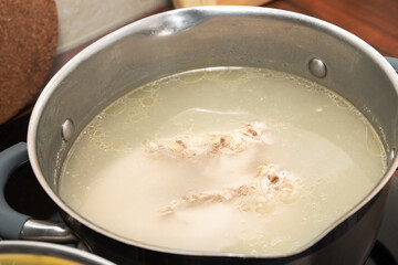 A healthy wholesome chicken breast broth is cooked on a stove in a saucepan
