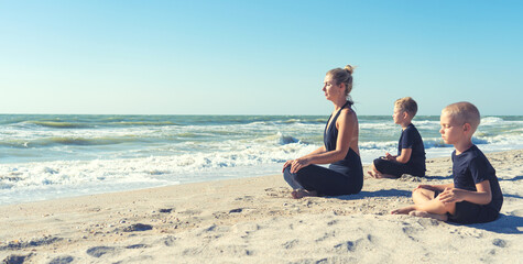 Mother and children do exercises on the beach, they meet the sunrise.Fitness, sport, yoga and healthy lifestyle concept.
