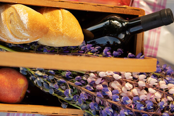 Picnic lunch food outdoors in summer in the Park. Basket with flowers, wine, peaches and baguettes