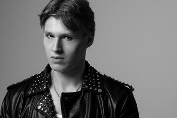 Young handsome man wearing black trendy leather jacket with rivets, posing on grey background. Black and white, monochrome close up studio fashion portrait. Copy, empty space for text