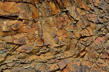 Cracked red rock. Rusty stones with sharp corners and fine red gravel. Plates of red, black and brown stone. Stone ready for mining.