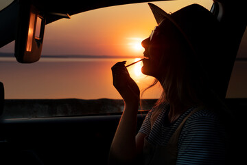 Beautiful woman paints her lips in the car .The evening sunset on the promenade	