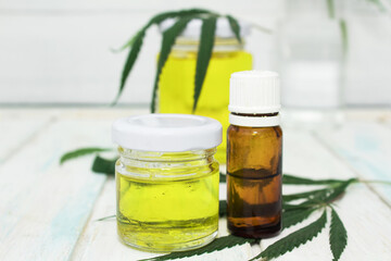 Hemp oil bottlse lies with green hemp leaves on white wooden background. Alternative medicine