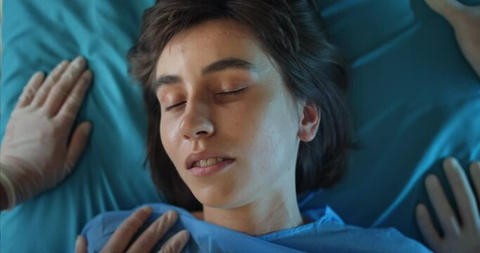 Millennial girl having seizure while lying on hospital stretcher. Close up view of paramedics checking pulse and holding young woman while going on ambulance. Concept of desease