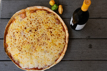 Top view of cheese pizza with bottle of wine on wooden table