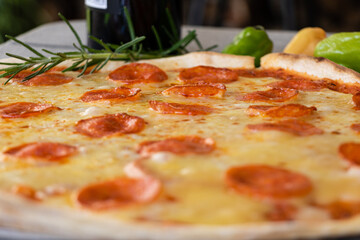 Close up of pepperoni pizza with fresh ingredients and bottle of wine in the background