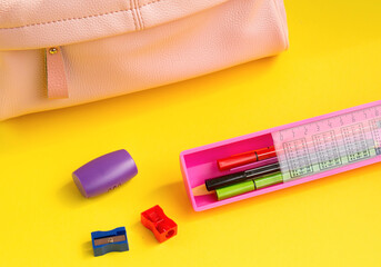 .Pink backpack and school items on a yellow background. Back to school concept. Close-up. Selective focus.
