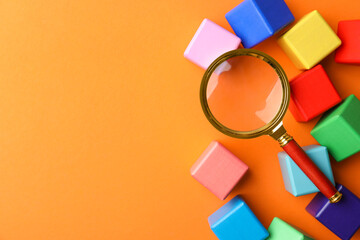Different colorful cubes and magnifier glass on orange background, flat lay with space for text....