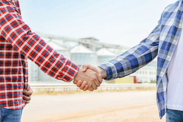 Businessmen shake hands against silos. Agriculture business © Atlas