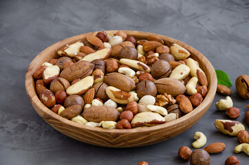 Mix of nuts in a wooden bowl on a dark concrete background. Healthy food concept. Horizontal, selective focus.