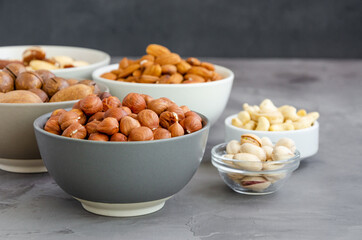Hazelnuts, almonds, Brazilian nuts, cashews, macadamia, pecans and pistachios in bowls on a dark concrete background. Healthy food. Horizontal, copy space.