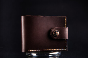 brown leather wallet made by hand on a glass stand on a black background close up