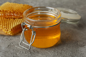 Honeycombs and glass jar with honey on gray background