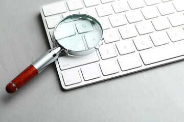 Magnifier glass and keyboard on light grey stone background, closeup. Find keywords concept