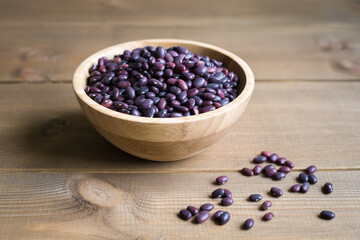 Fototapeta na wymiar Purple raw beans in a bowl on a wooden background. The grains are scattered nearby. Close up composition.