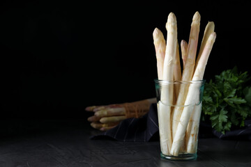 Fresh white asparagus in glass on table against black background. Space for text