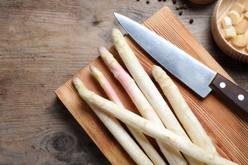 Fresh white asparagus, cutting board and knife on wooden table, flat lay