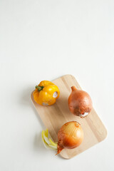 The whole spoiled, rotten onions and bell peppers lie on a wooden board on a white concrete background. Mold on vegetables. Flat lay, close up with place for text composition.