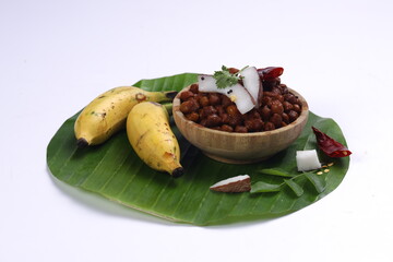 Kadala curry or Bengal gram curry,home made chana curry arranged in a wooden bowl and garnished with coconut slices, dry chilli and curry leaves on banana leaf with pair of banana besides