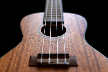 Close up view of a wooden ukulele body isolated on a black background.