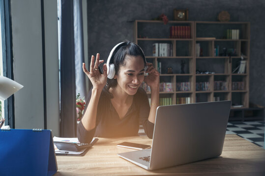 Businesswoman working online at the home office via laptop. Asian young entrepreneurs watching webinars and talking during meeting video conferences calls with team, and using mobile phone.