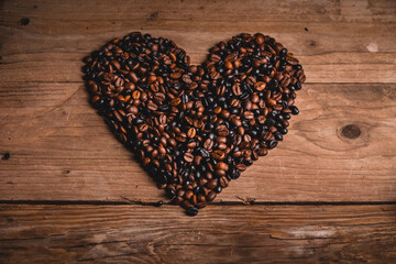Top view of aromatic coffee grains arranged on wooden table in shape of heart