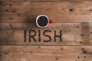 Top view composition of red mug with roasted aromatic coffee placed on wooden table above inscription irish made with coffee beans