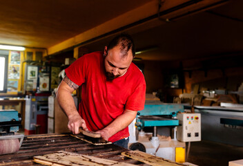 Busy male woodworker standing at workbench and polishing timber plank with brush