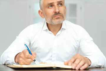 From below of excited charismatic ethnic guy in white shirt with pen in hand creating project at workplace