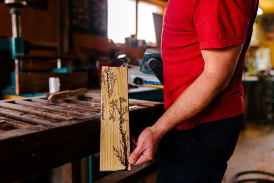 Side view of crop male pyrographer standing in workshop and demonstrating amazing woodwork decorated with burn marks