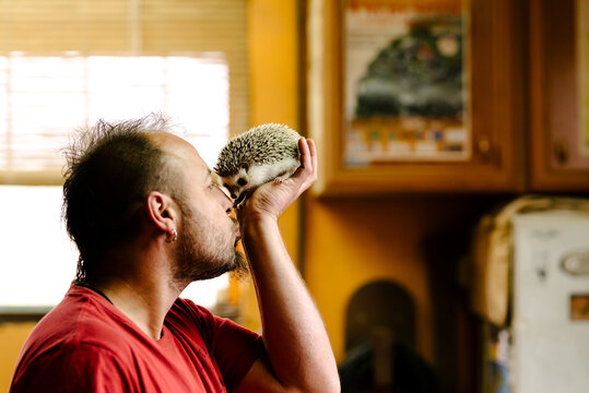 Side view of male with piercing standing in kitchen with cute hedgehog