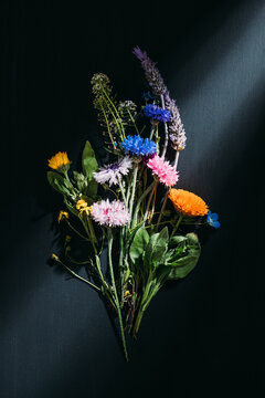 From above of bouquet of colorful flowers placed in glass cup on black background in studio