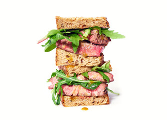 Close up of a pile of beef steak sandwich with arugula and mustard dressing against bright background