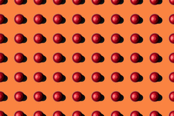 Top view of red coffee pods placed in even rows as seamless pattern on orange background