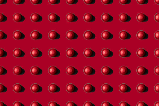 Top view of red coffee pods placed in even rows as seamless pattern on red background