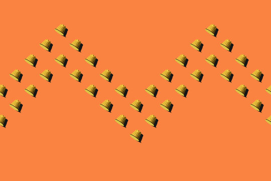 Top view of yellow coffee pods placed in even rows as seamless pattern on orange background