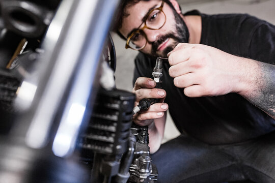 Serious male mechanic repairing dirty spark plug of motorbike while working in garage