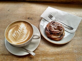 A latte coffee and danish cinnamon bun with a wooden table background, in a coffee shop or cafe.