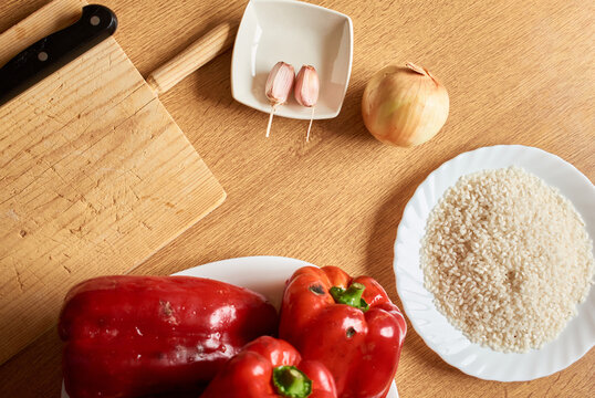 From above of wooden table with fresh red peppers placed near rice and condiments for cooking stuffed peppers