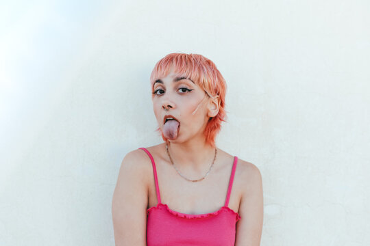 Young female standing near stone wall and making funny faces with with tongue out looking at camera