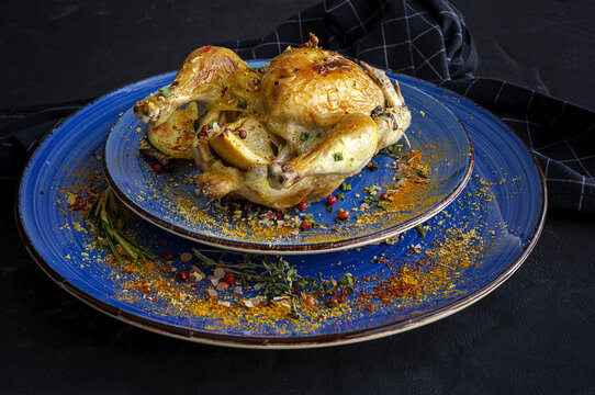 From above of ceramic plates with tasty French coquelet with golden surface garnished with slices of roasted potatoes and seasoned with fresh rosemary and different spices