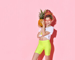 Teenage female with african pigtails, in sunglasses. She is holding pineapple and smiling, posing on pink background. Close up