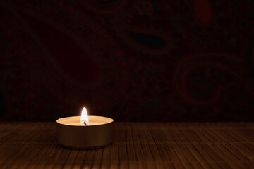 Burning tea light on the wooden table in darkness for copy space.