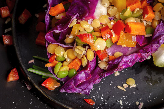 From above of colorful purple cabbage leaf filled with mix of peppers and lentils near slice of fresh lemon and Himalayan salt on dark plates